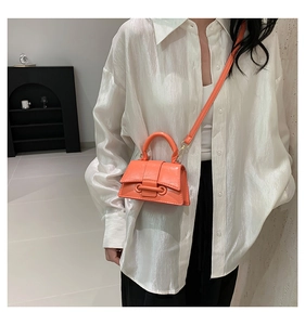 Detail of a bright orange crossbody bag with a structured handle and glossy finish