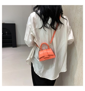 Detail of an orange-red mini crossbody bag with unique flat ring buckle on model