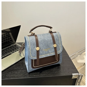Detail of vintage denim and brown leather handbag with gold buckle on a desk