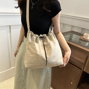 Large cream nylon bucket bag with drawstring closure and side pockets on a model