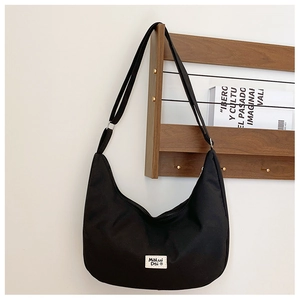 Close-up of black canvas saddle bag featuring a white woven logo tag and adjustable strap