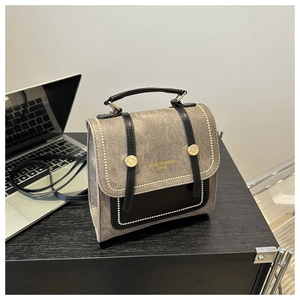 Detail of retro denim grey tote bag with gold rivets and black leather handles on desk