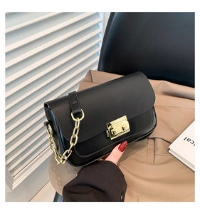 Detail of a black matte rectangular bag with a golden push-lock and metal chain strap