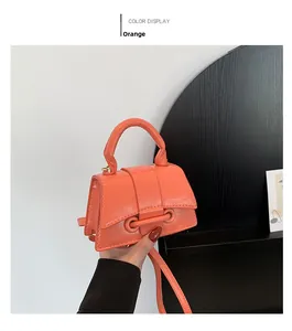 Detail of an orange mini leather handbag with glossy finish and modern buckle design