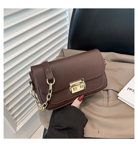 Detailed view of dark brown leather handbag with gold metal clasp on a trench coat