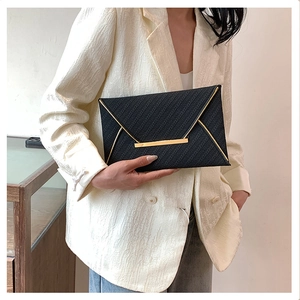 Détail d'une pochette enveloppe noire avec bordure dorée et texture tissée sur mannequin
