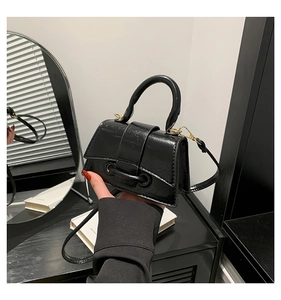 Detail of a black patent leather mini handbag with gold hardware and top handle