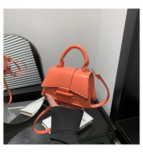 Detail of orange patent leather mini handbag with top handle and crossbody strap