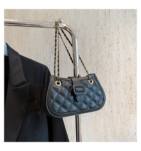 Detail of black quilted leather shoulder bag with gold chain strap and luxury buckle