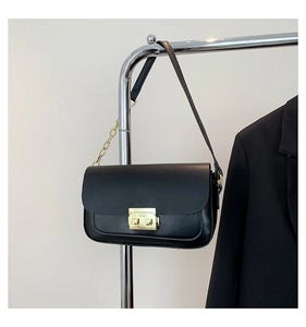 Detail of black matte shoulder bag with gold chain strap and metal clasp on a hanger