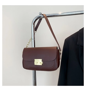 Detail of a vintage dark coffee leather flap bag with gold clasp on a metal rack