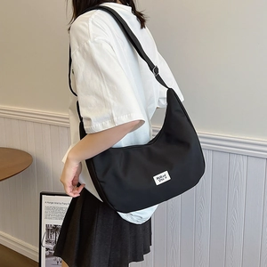 Minimalist black crescent shoulder bag with adjustable strap worn by model in a room