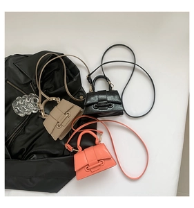 Flat lay of mini trapezoid crossbody bags in black, khaki, and pink on a leather jacket