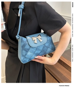 Detail of blue denim shoulder bag with silver bow hardware and quilted texture pattern