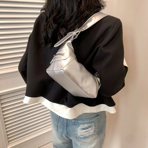 Silver metallic crescent shoulder bag with wide strap worn by a model in casual setting