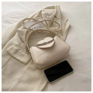 Detail of cream crossbody bag featuring heart flap and silver metallic bead chain decoration