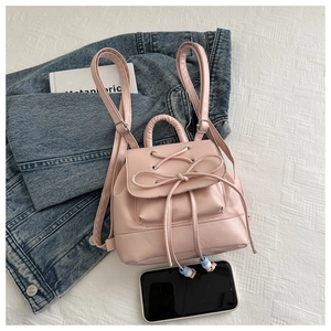 Detailed close-up of a mini pink leather backpack with bow tie laces and a smartphone for scale