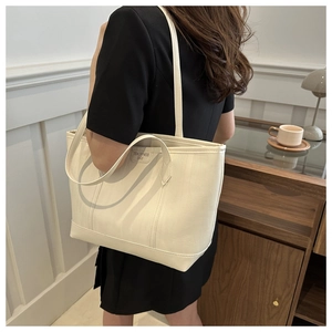 Vista laterale di una grande borsa tote bianco crema in ecopelle martellata su modella