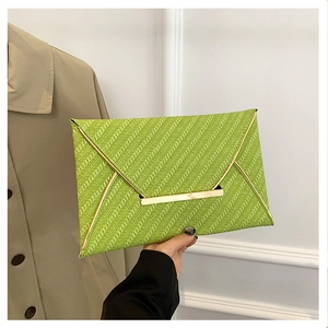 Détail d'une pochette enveloppe vert vif avec garniture en métal doré et texture tressée