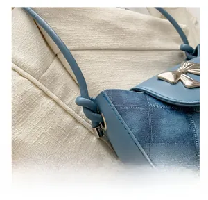 Detail of light blue crossbody bag with silver bow hardware and patchwork texture
