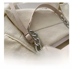 Dettaglio della tracolla in pelle regolabile con fibbia argentata e catena sulla borsa beige