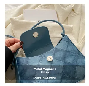 Detailed macro view of the metal magnetic snap closure on a denim texture square bag
