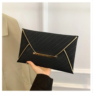 Détail d'une pochette enveloppe noire avec texture tressée et bordures métalliques dorées
