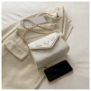 Detail of white quilted crossbody bag with gold chain strap on textured fabric