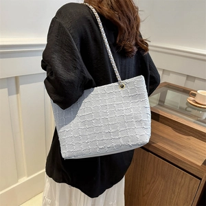 Light blue tweed tote bag with metal chain strap worn by a model for a casual look