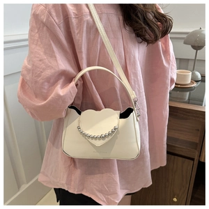 Detail showing creamy white heart-shaped crossbody bag with metallic bead trim on a model