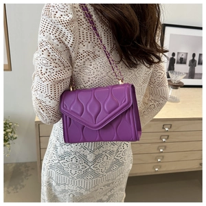 Detail of purple crossbody bag with teardrop stitching and gold chain on model