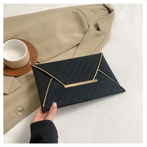 Détail d'une pochette enveloppe noire à texture tissée et bordures dorées chic