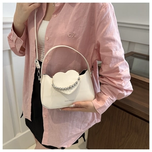 Detailed view of white heart-flap bag with silver beads held by model in pink shirt
