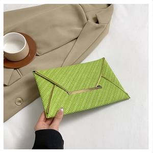 Détail macro de la texture tissée verte et bordure métallique dorée sur la pochette enveloppe