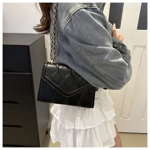 Detail of black quilted leather shoulder bag with gold chain strap worn by model