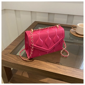 Detail of fuchsia chain bag featuring wavy quilted texture on wood glass table