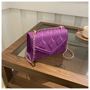 Detail of purple wavy quilted crossbody bag with gold chain strap on a wooden table