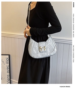 Silver pleated metallic shoulder bag with bow hardware shown on a black dress