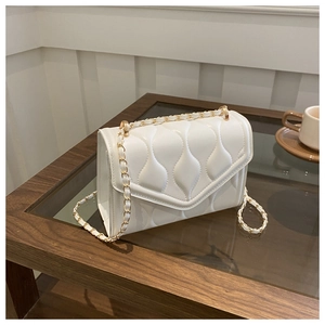 Detail of white quilted crossbody bag with gold chain strap on a wooden table