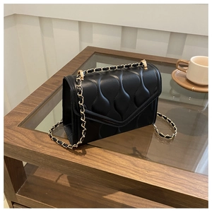 Detail of black quilted shoulder bag with wave pattern and gold-tone chain strap