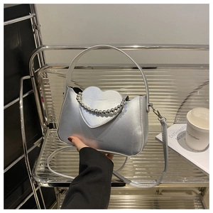 Detail of silver heart-flap handbag featuring a beaded chain handle and metal texture