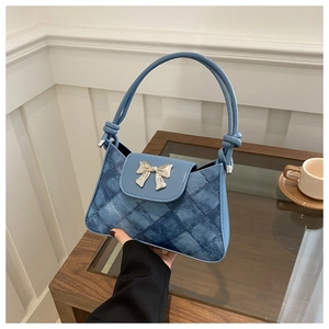 Detail of denim blue checkered shoulder bag with silver bow hardware on a wooden table