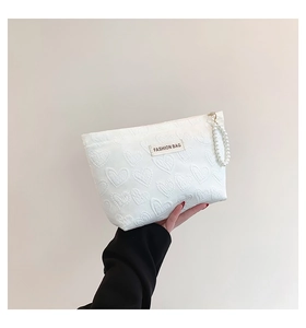 Detail of white heart-embossed quilted makeup bag with pearl strap and fashion label