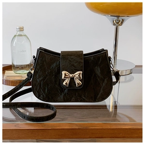Dettaglio di borsa nera increspata con elegante chiusura metallica a fiocco dorato lucido