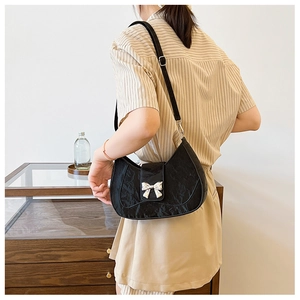 Detail of black pleated crescent underarm bag featuring a metallic silver bow buckle