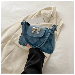 Close-up of blue quilted leather shoulder bag with a metal bow buckle and knot strap detail