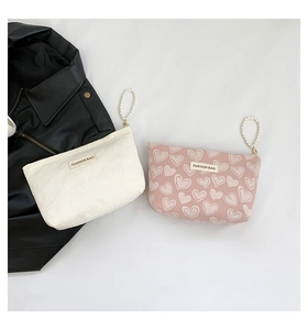 Detail view of heart-embossed canvas makeup bags in beige and pink with pearl wristlets