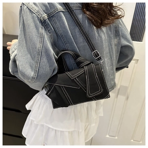 Detail of black denim crossbody bag with contrast white stitching on a female model
