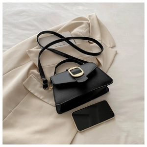Detail view of black lychee leather bag with gold buckle on a beige blazer and a phone