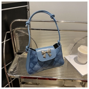 Close-up of blue quilted denim shoulder bag featuring a silver metal bow accent